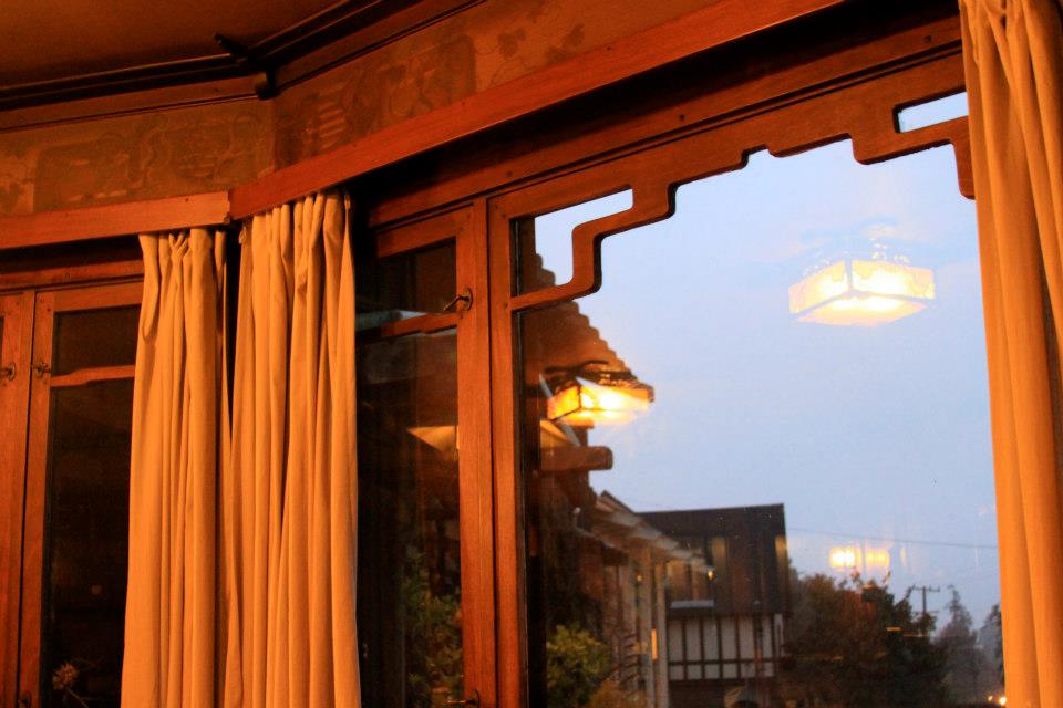 Evening view from Thorsen House dining room bay window showing cloud lift art glass, timber frame, and illuminated exterior