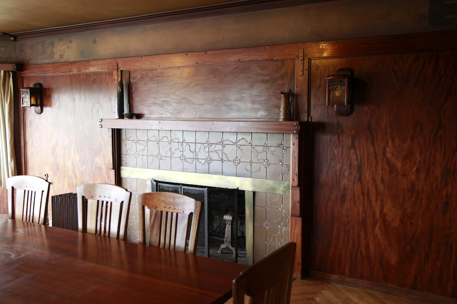 Thorsen House dining room fireplace with geometric tile surround, mahogany mantel, flanking sconces, and original furniture