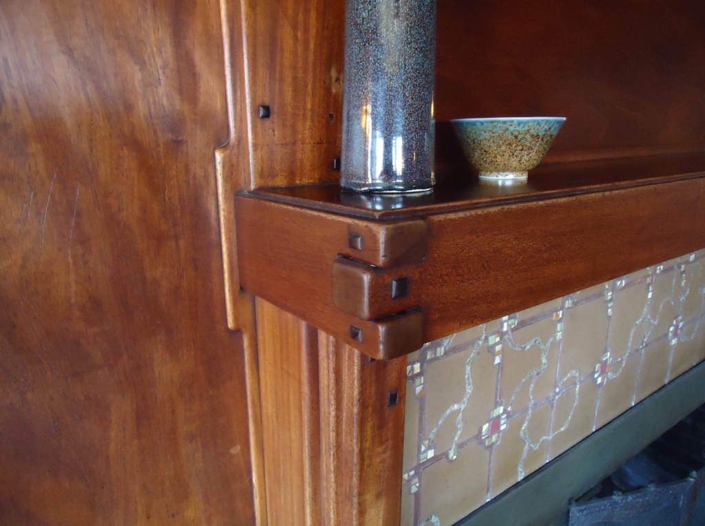 Close-up of Thorsen House dining room fireplace mantel with stepped corbels, ebony pegs, and ceramic pottery display