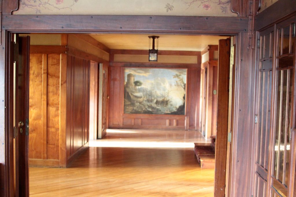 View through Thorsen House entrance hall showing harbor scene painting in box frame, hanging lantern, and wood paneling