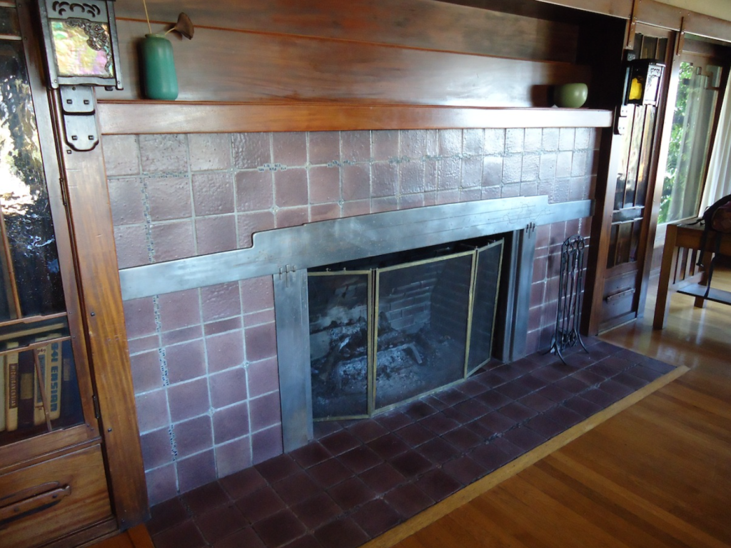 Thorsen House living room fireplace with textured tile surround, copper mantel, flanking sconces, and recessed hearth