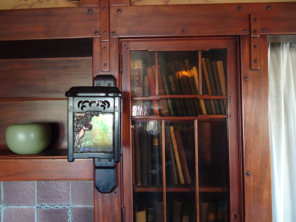 Thorsen House living room fireplace mantel sconce with art glass panel, built-in bookcases, and ceramic pottery