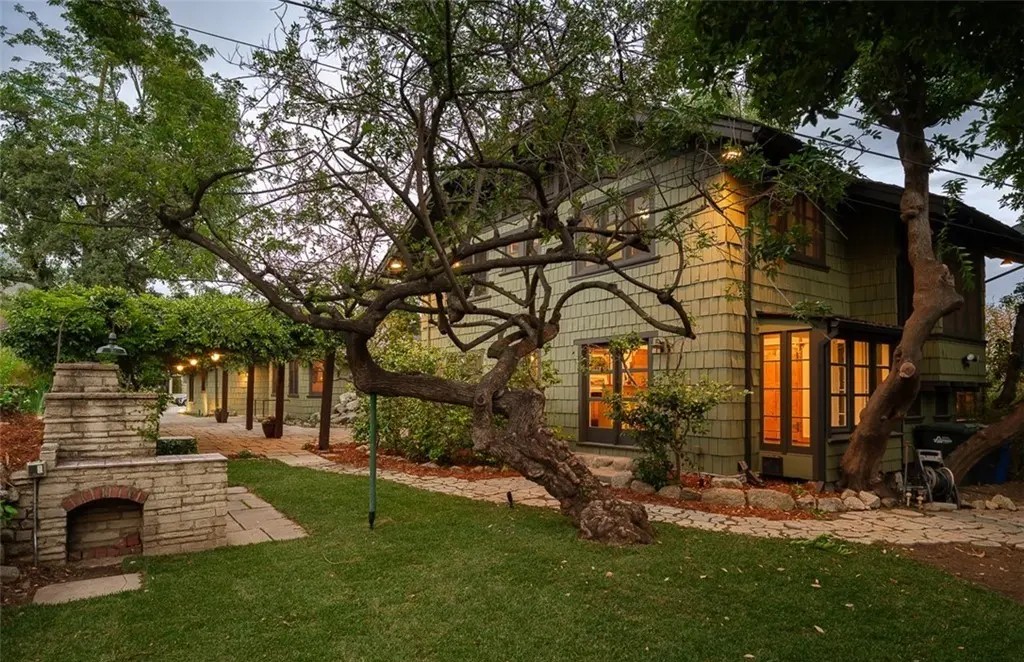 Backyard view of Edgar W. Camp house with outdoor brick fireplace, mature oak tree, and shingle siding at twilight