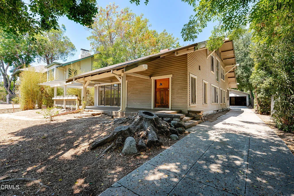 Driveway view of Francis F. Rowland house with natural wood siding, hipped roof, timber pergola, and rock garden feature