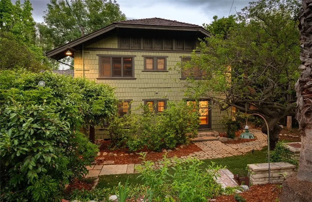 Two-story facade of Edgar W. Camp house with decorative attic vents, shingle siding, and lush garden landscaping