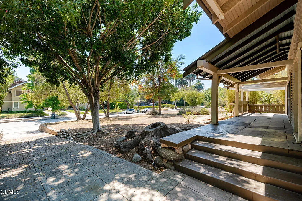 Front porch of Francis F. Rowland house with exposed timber pergola, wide steps, rock garden, concrete walkway, and mature street trees