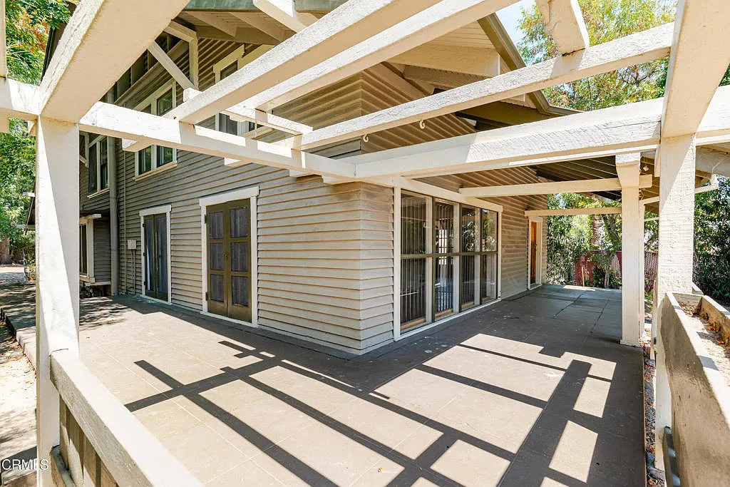 View under white timber pergola of Francis F. Rowland house showing exposed beams, concrete porch floor, two-tone wood siding, and large windows