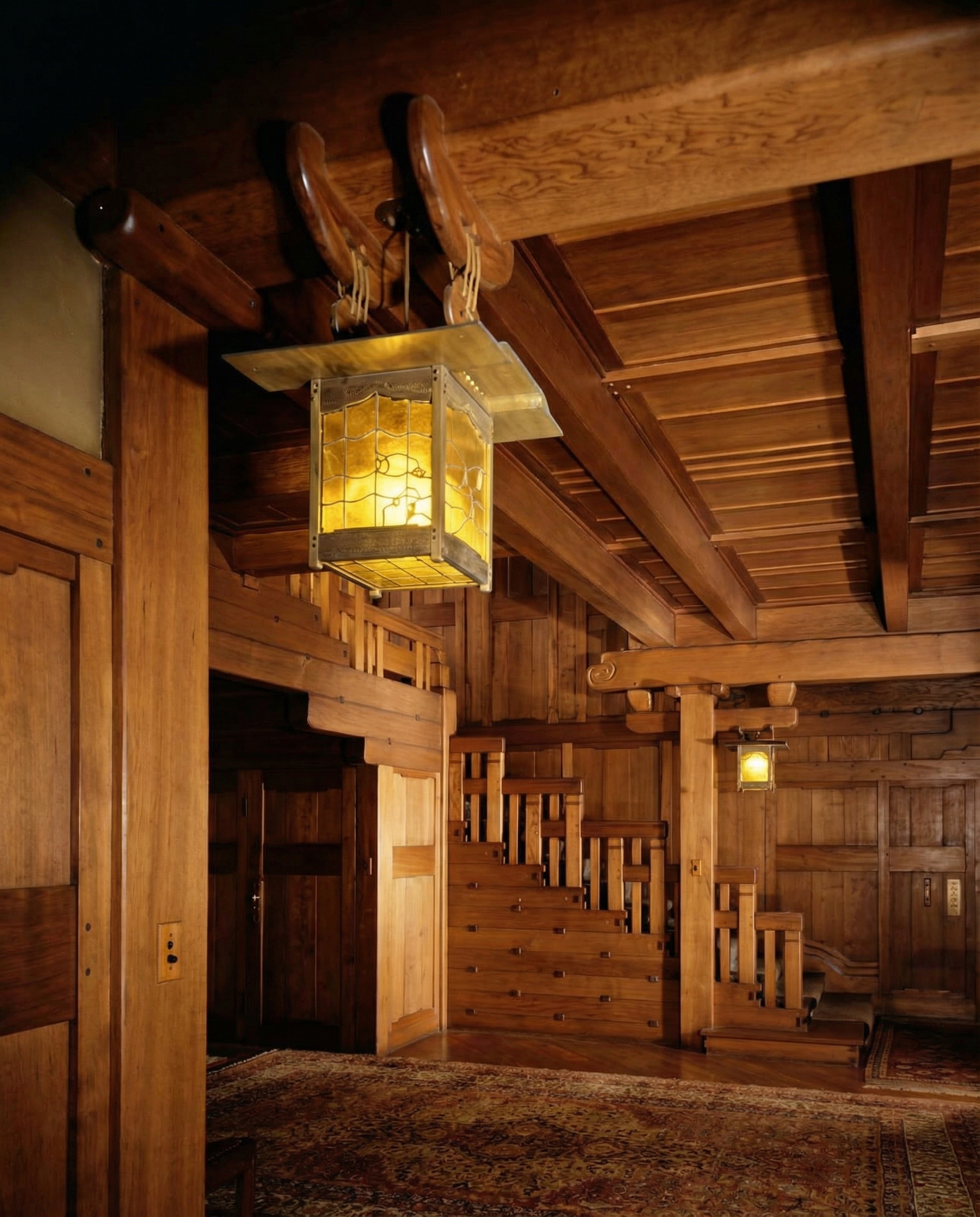 Early colorized photograph of the entry hall of the Robert R. Blacker House, a mahogany-and-leaded-glass hanging lantern suspended from carved wooden brackets, with the stepped stair railing beyond.