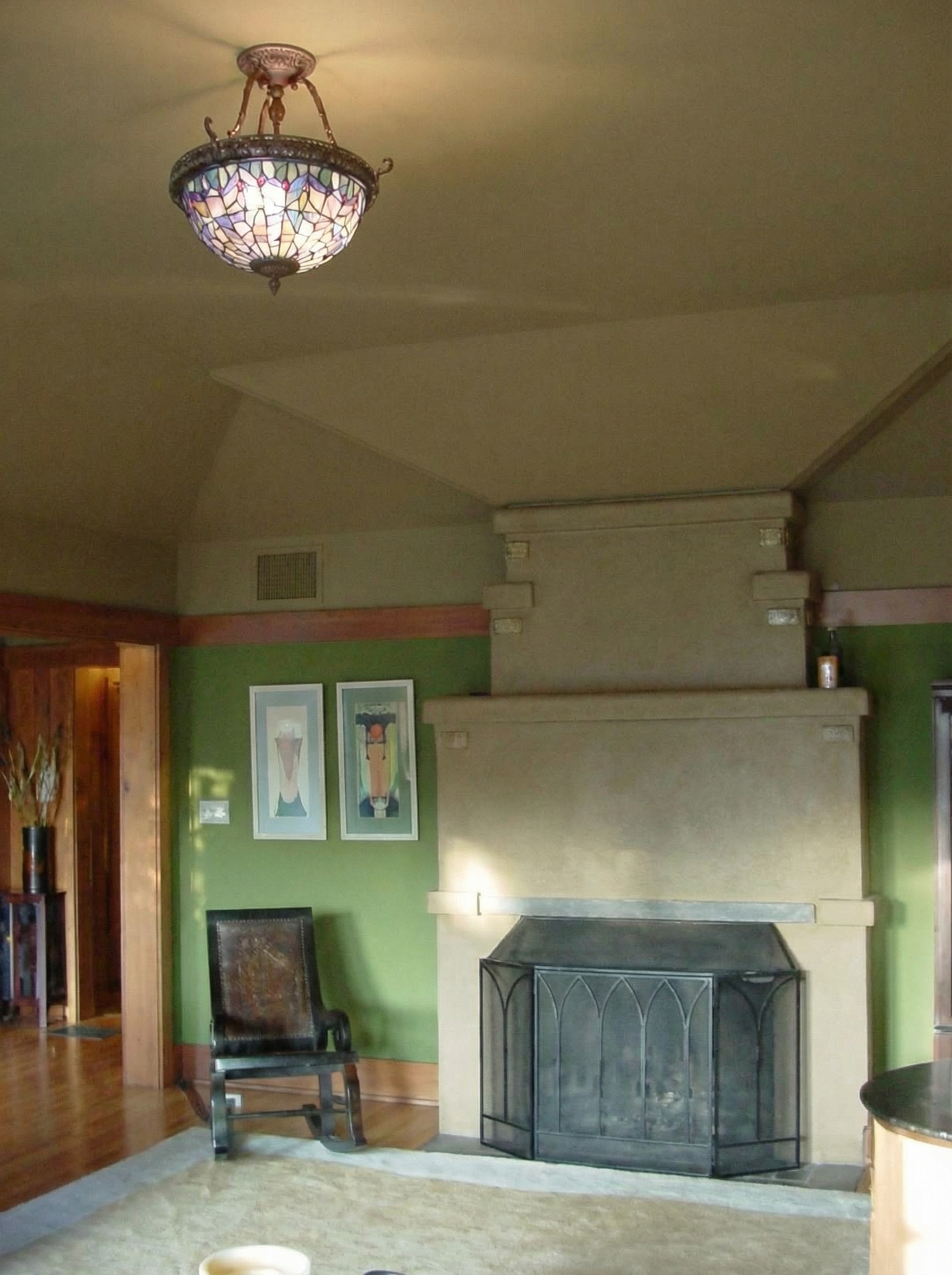 Interior view of the living room at Charles Greene's own Pasadena house showing the partial octagonal bay projecting outward with four window-walls of multipaned wood-framed casements opening toward the Arroyo Seco, with low wood paneling, a beamed ceiling, and the Western afternoon light entering from three directions