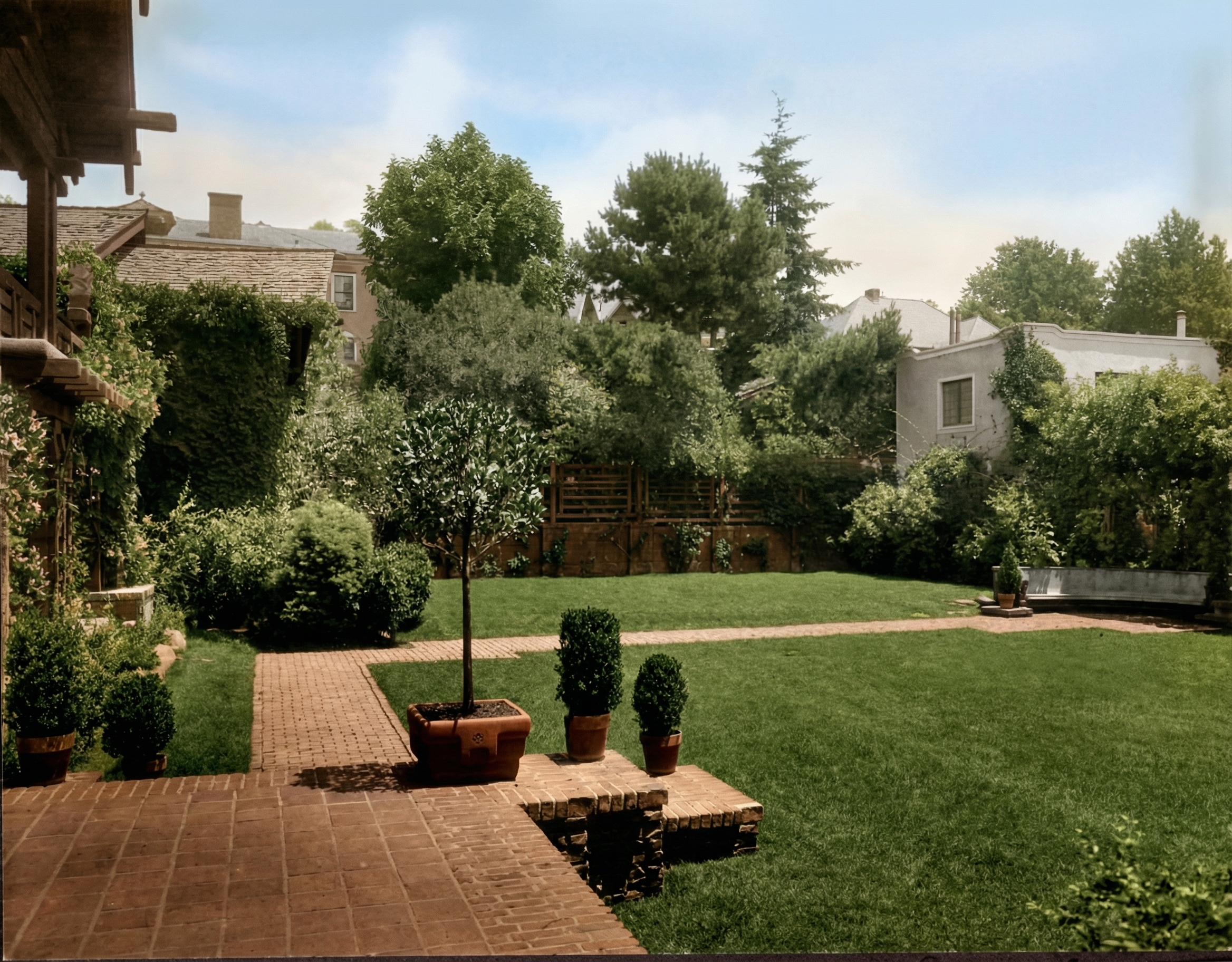 Historic view of Thorsen House backyard looking east, showing brick terrace, fountain, lawn, and garage structure