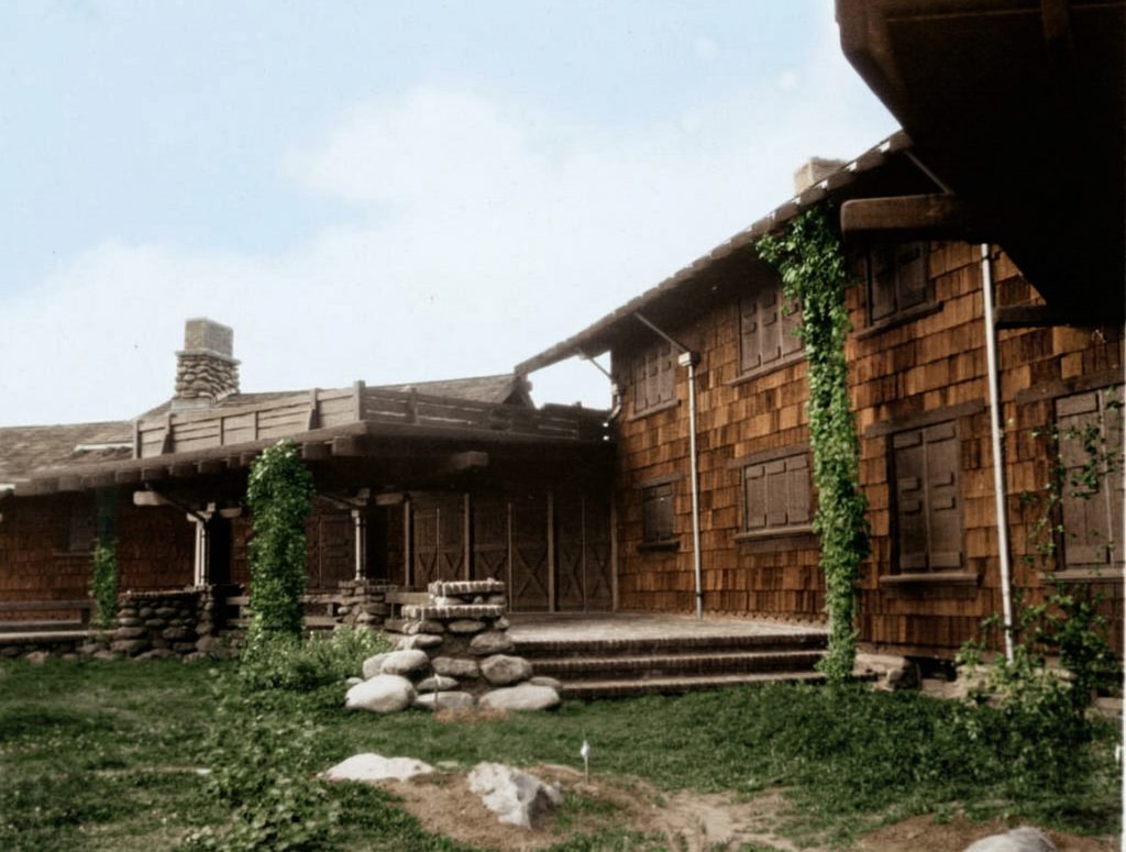 Vintage photo of east rear view showing wood shingle siding, river rock terraces, and climbing vines on the rustic Pratt House.