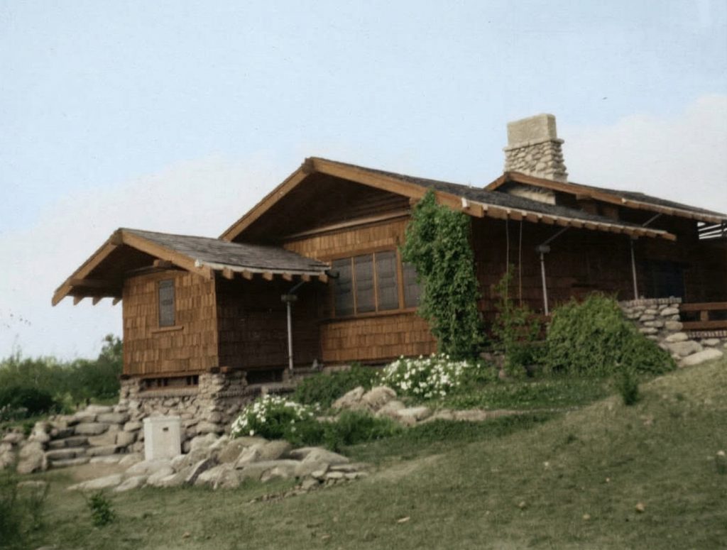 Early photograph of east view showing wood shingle siding, river rock foundation, and climbing vines on the hillside setting.