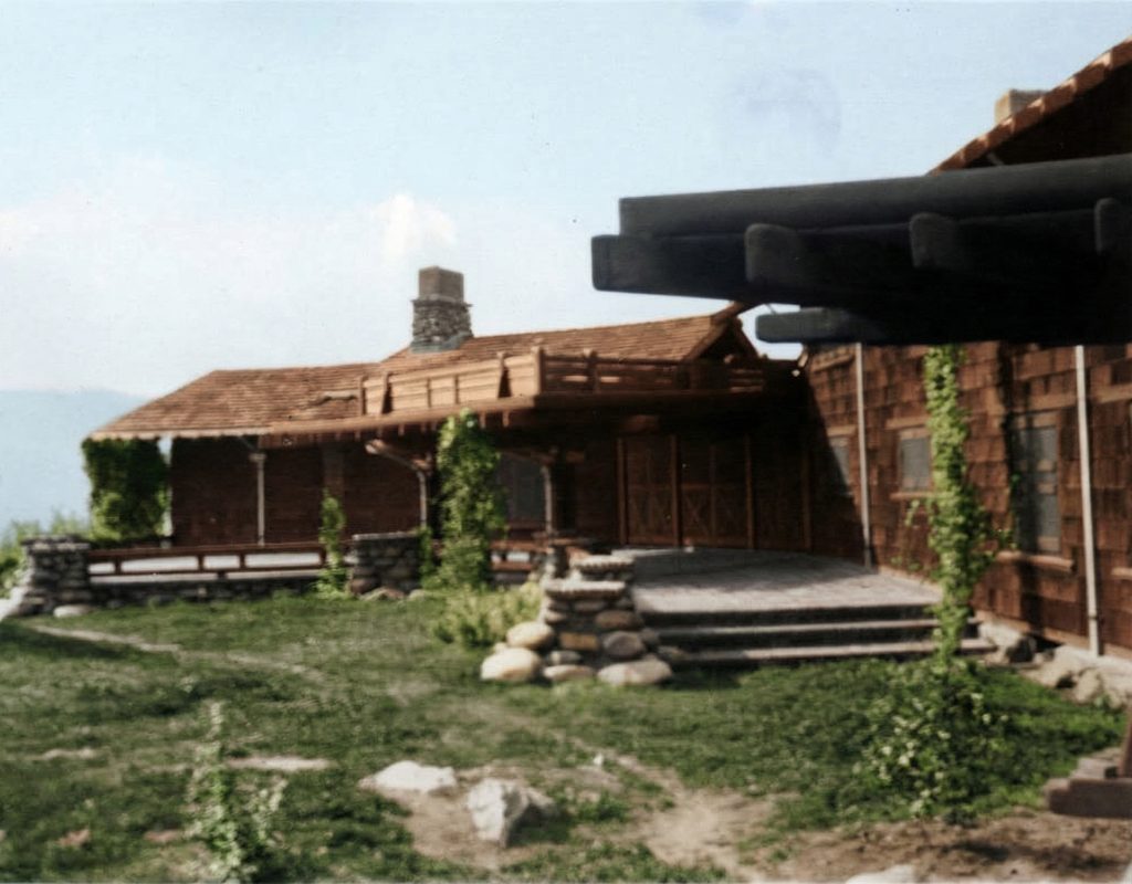 Early photograph showing rear terrace with dramatic cantilevered beams, river rock columns, and V-shaped wings embracing the landscape.