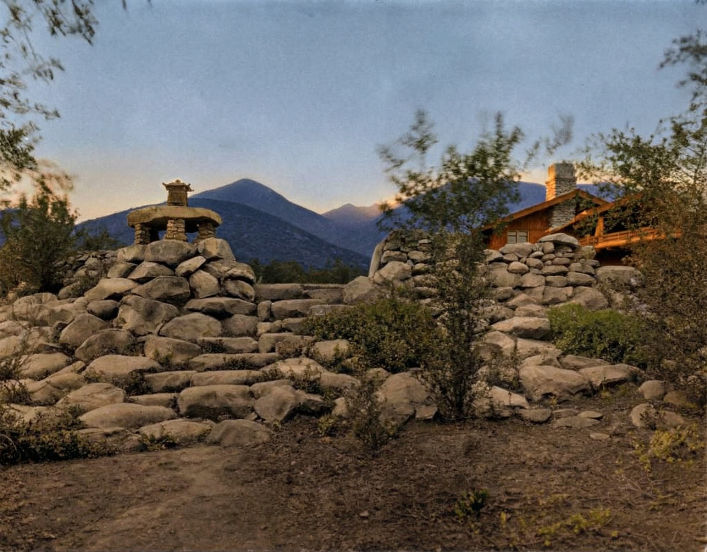Historic photograph of one of the cobbled river-rock retaining walls and stone steps on the grounds of the Pratt House, with mature plantings descending the slope.