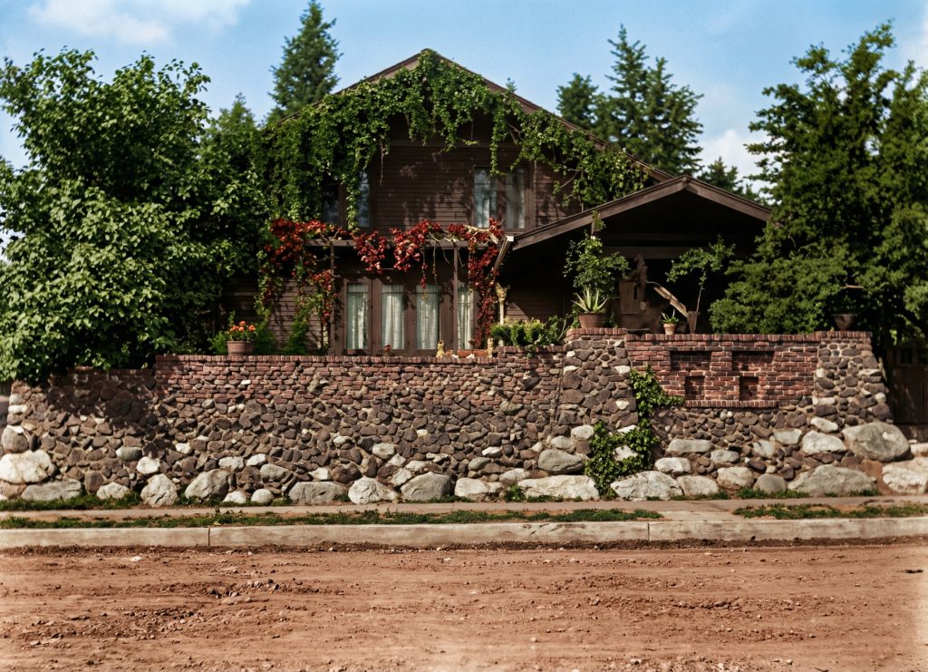 Early photograph of the van Rossem-Neil House featuring its cobblestone retaining wall, climbing vines, and wood siding.