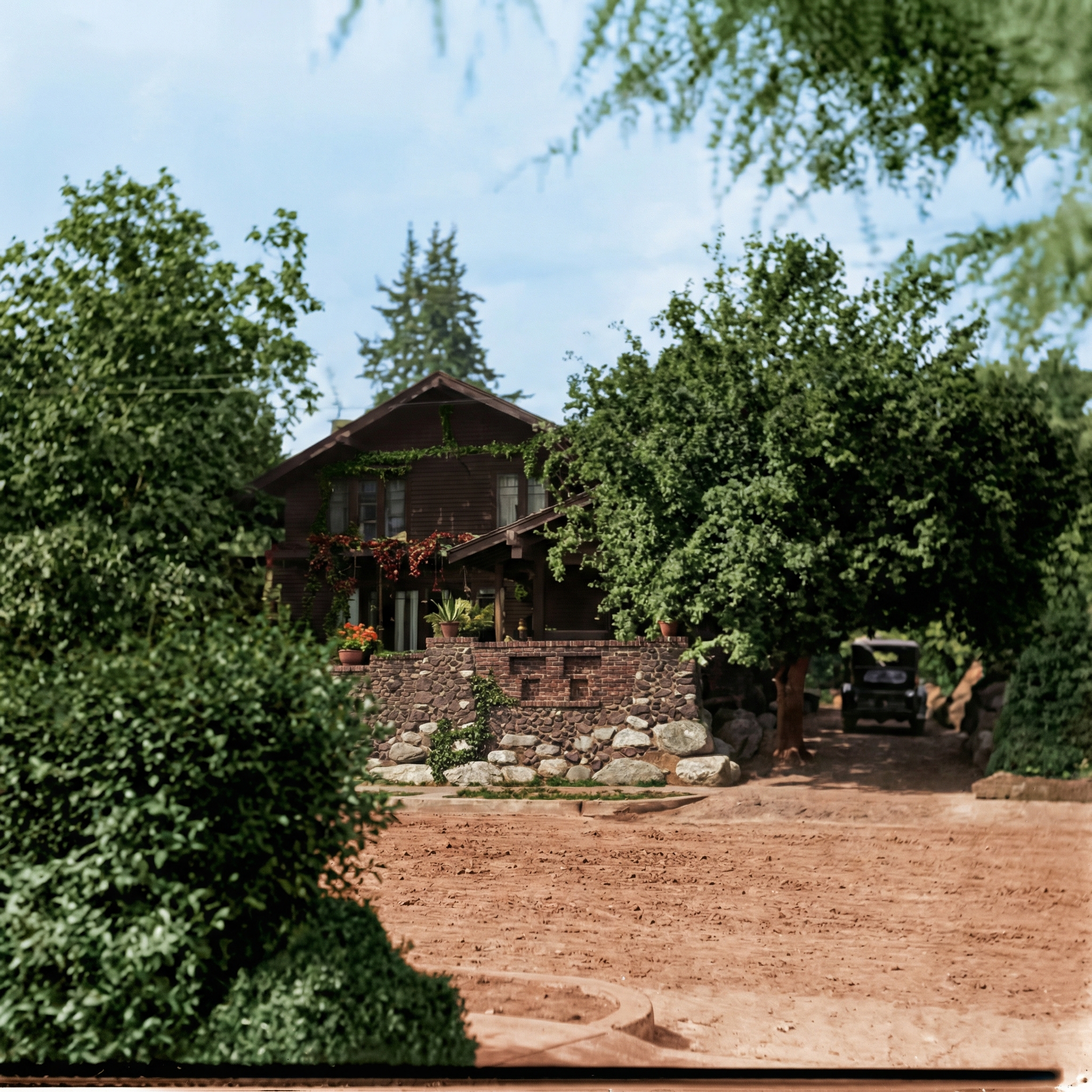 A frontal view of the shingled Van Rossem-Neill house showing the broad low gable, the deep porch, and the boulder retaining wall along the street.