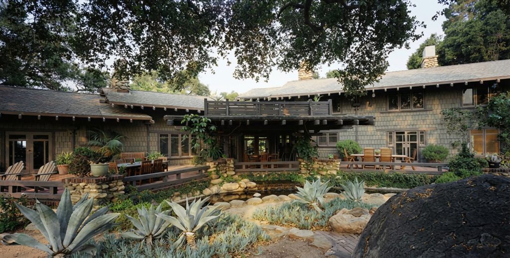 Expanded rear terrace view of The Charles M. Pratt House showing stone paving, columns, and surrounding garden landscape