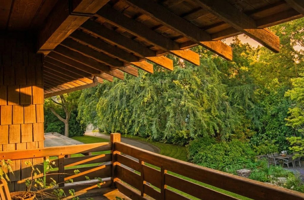 Open-air sleeping porch with exposed timber rafters and garden views at The Margaret B. S. Clapham Spinks House.