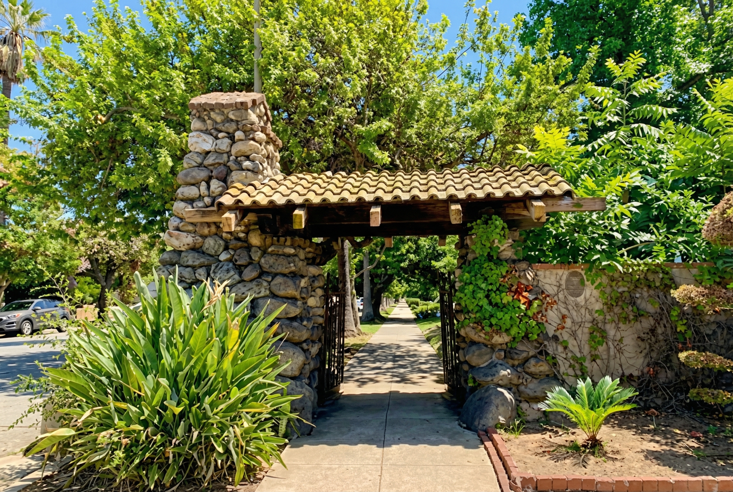 The Oaklawn Portals featuring a cobblestone tower with clay tile roof and metal pedestrian gate amid lush greenery.