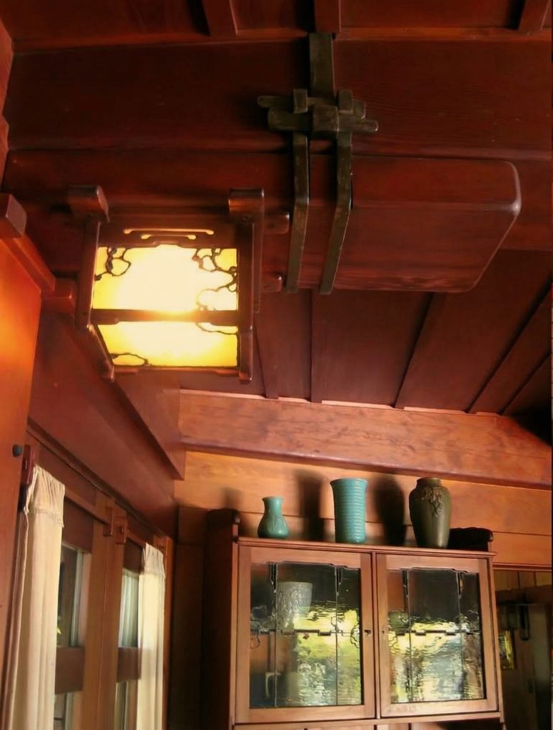 Interior beam lighting at The Charles M. Pratt House showing exposed wood beams and Arts and Crafts light fixtures