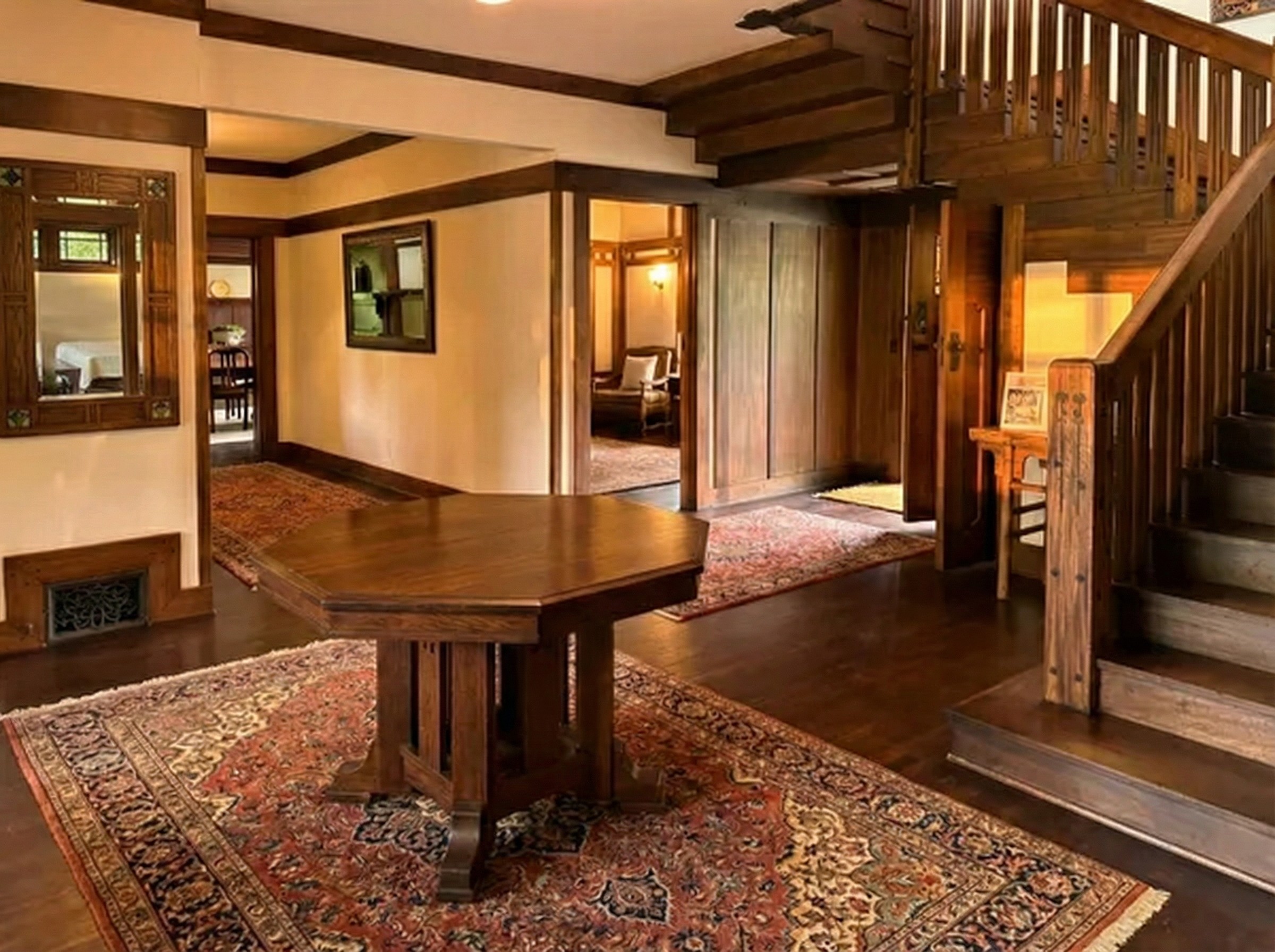 The entrance hall of the Stimson House: a paneled wood interior with an open staircase, dark beams, a leaded glass window on the stair landing, and a built-in bench at the foot of the stair.