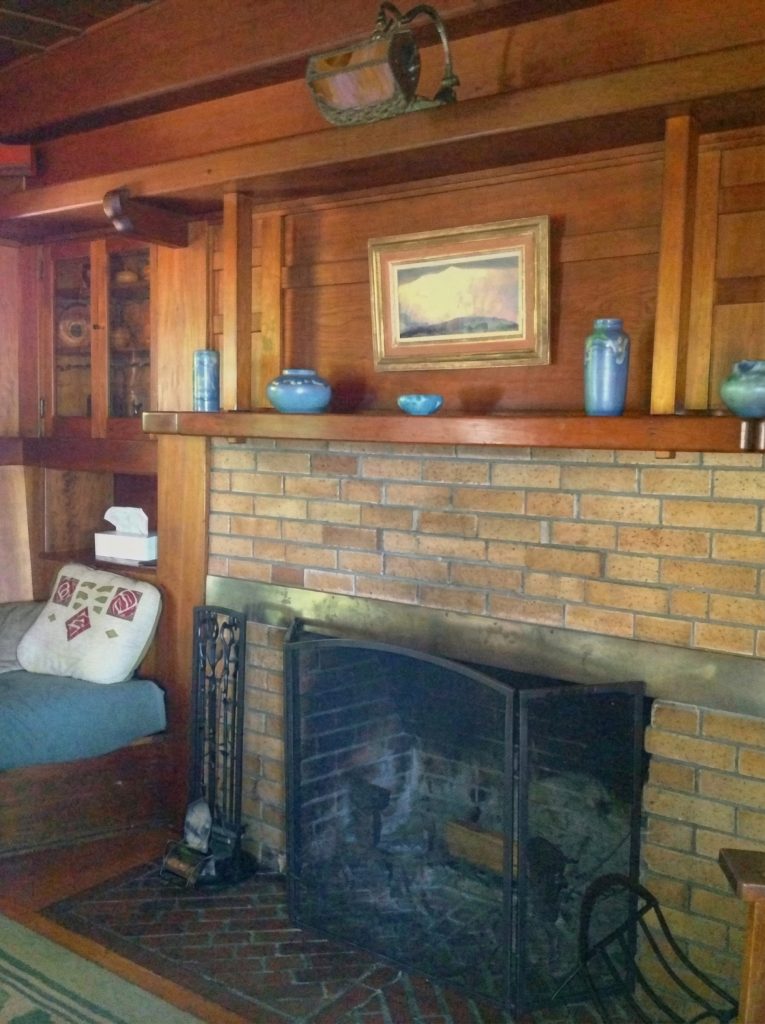 Living room fireplace at The Charles M. Pratt House with stone surround, wood mantel, exposed beams, and inglenook seating