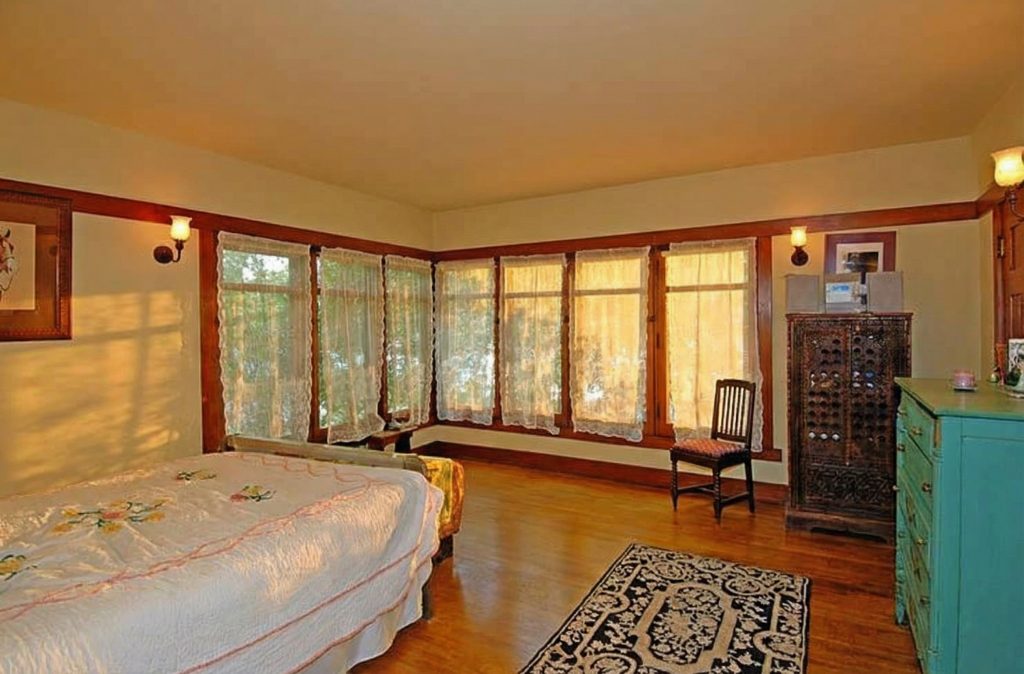 A serene bedroom in The Caroline S. de Forest House, with a wall of windows, lace curtains, and antique furnishings.