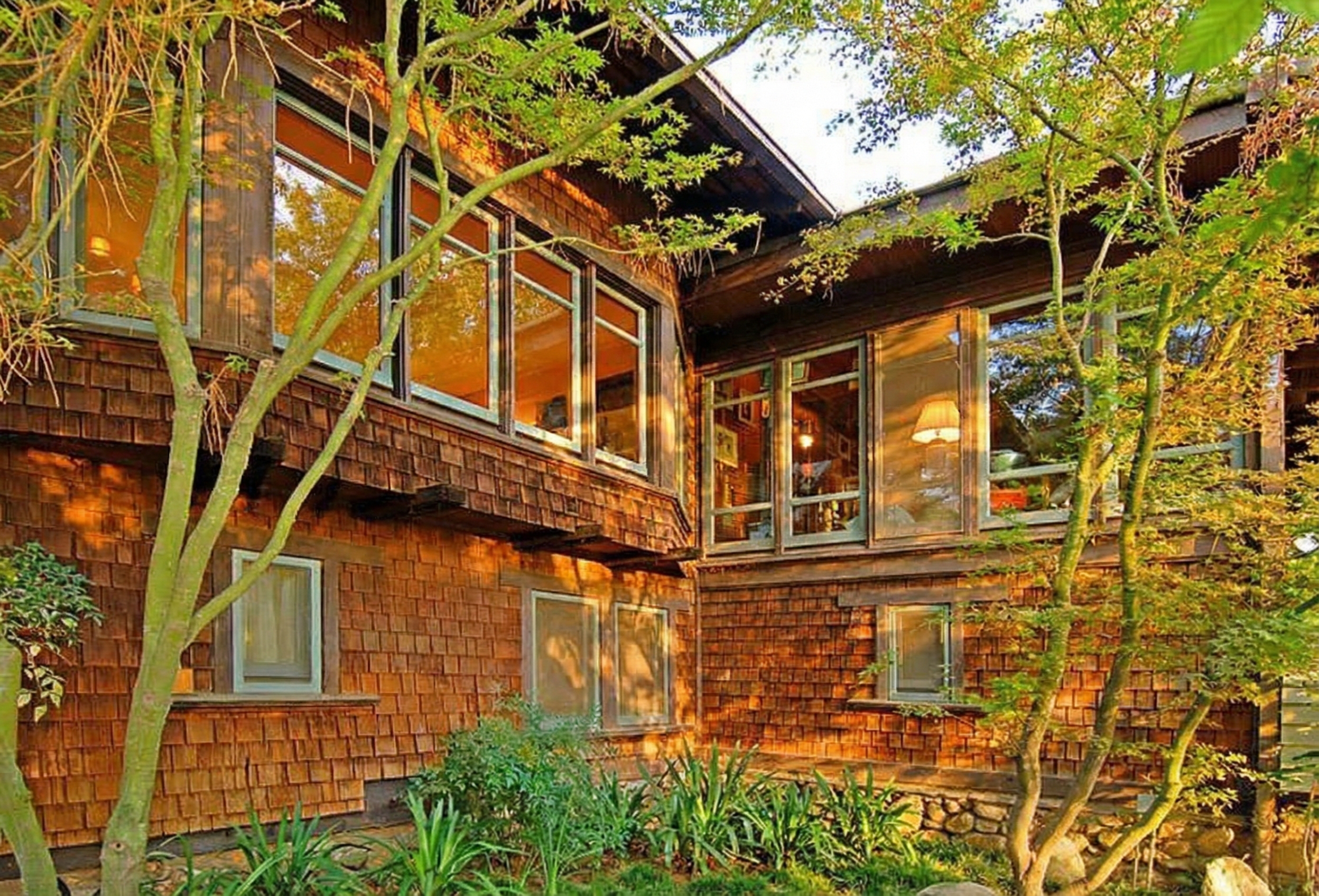 The shingled exterior of The Caroline S. de Forest House, nestled among lush greenery and mature trees, showcasing its Craftsman design.