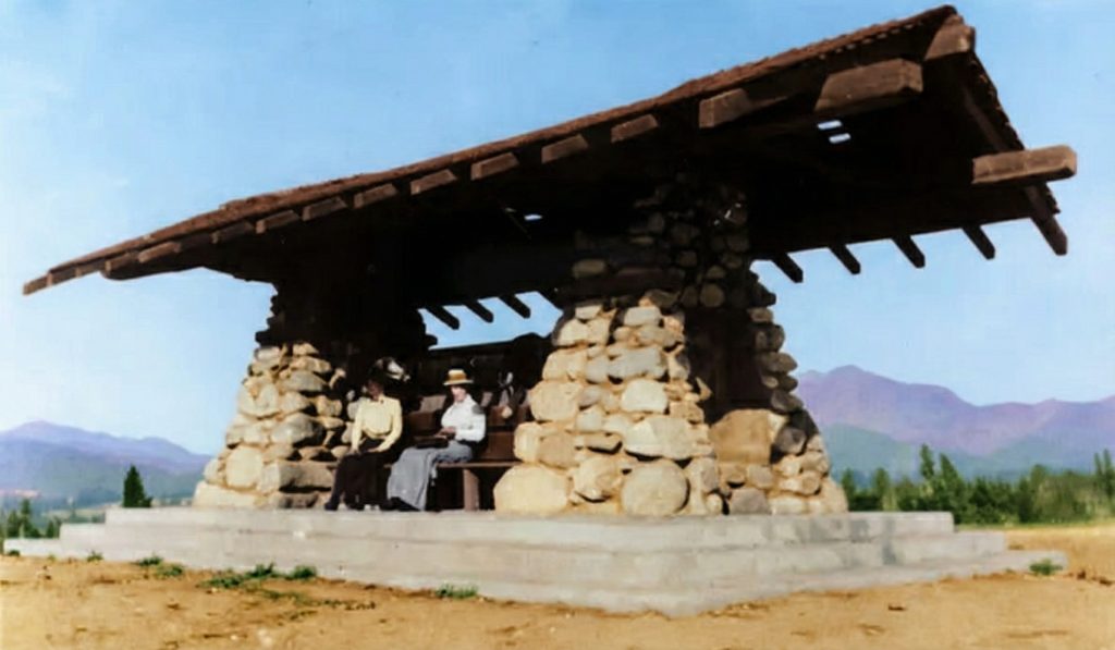 Front view of Greene & Greene's 1907 pavilion with two visitors seated on built-in bench between stone pillars
