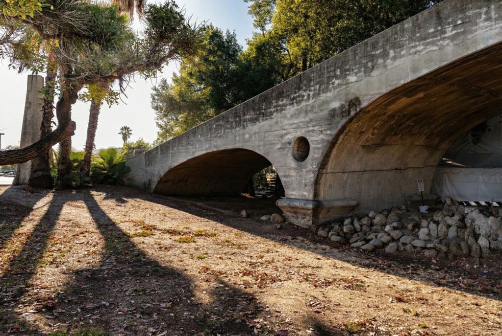 The Oaklawn Bridge's graceful concrete arches and circular spandrel openings framed by mature palm trees in South Pasadena.