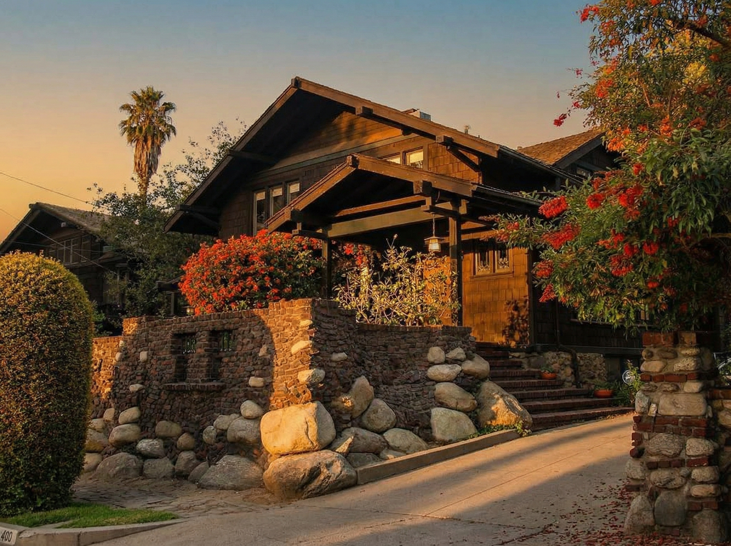 The van Rossem-Neil House at golden hour, showcasing its exposed timber beams, cedar shingles, and arroyo stone wall.