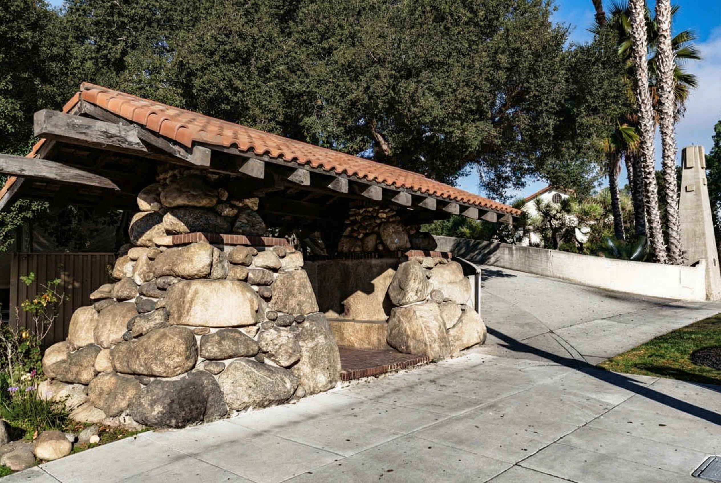 The small boulder and redwood waiting station at the foot of the Oaklawn Bridge, with its heavy timber roof and tile covering