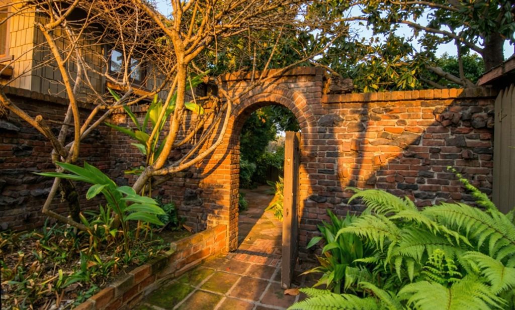 Clinker-brick garden wall opening at The Earle C. Anthony house revealing the landscaped grounds and mature plantings