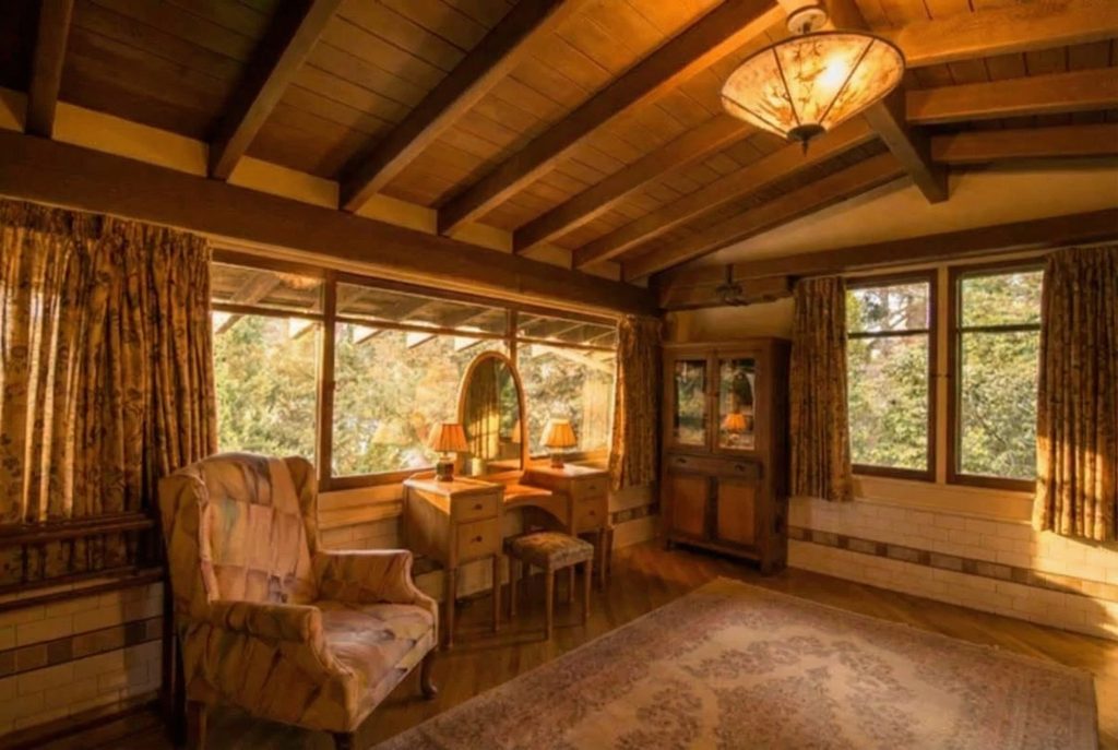 Second floor bedroom at The Earle C. Anthony house featuring original wood trim, beamed ceiling, and warm natural light