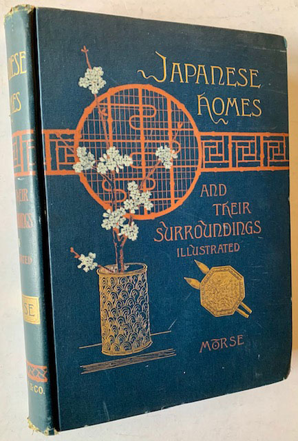 Photograph of the original 1885 hardcover edition of Edward S. Morse's "Japanese Homes and Their Surroundings," with its distinctive blue cloth binding featuring an orange medallion containing a stylized cherry blossom branch in a Japanese basket, the foundational English-language reference on Japanese domestic architecture