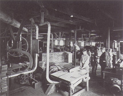 Black and white photograph of the interior of the Hall Manufacturing Company woodworking shop in Pasadena, California, showing workers, milling machinery, and stacked lumber, circa early 1900s