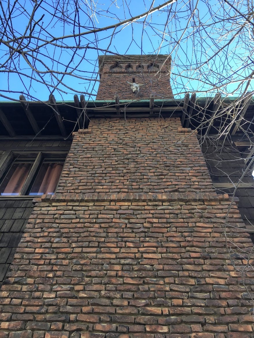 Massive clinker brick chimney of the Thorsen House climbing three stories along the Bancroft Way elevation, the brickwork mottled with over-fired discards in dark red and black tones against the brown shingle wall