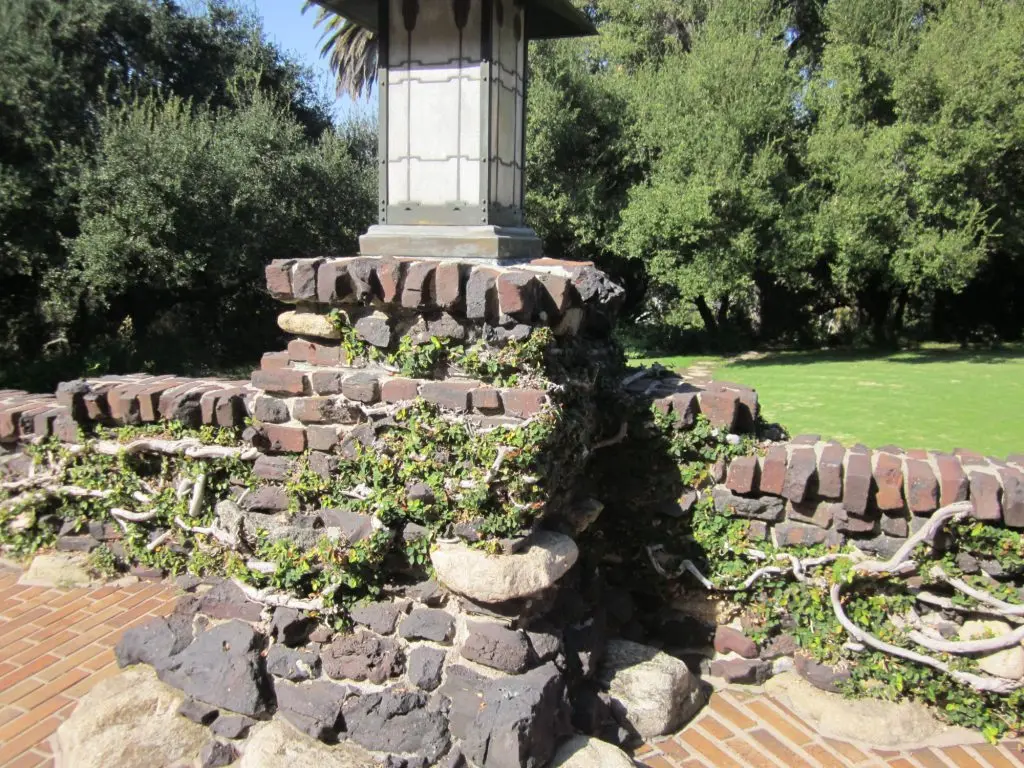 Detail of a Greene and Greene clinker brick and arroyo stone pier and low wall at the David B. Gamble House, showing the irregular dark over-fired bricks combined with rounded river stones and a craftsman art glass lantern above