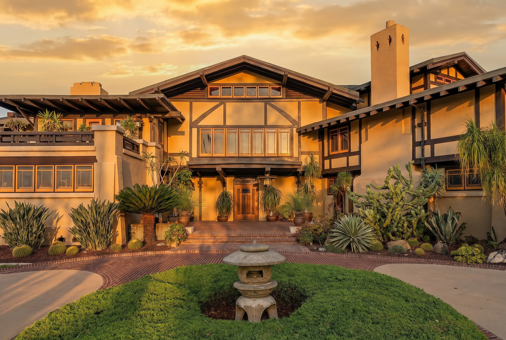 Sunset photograph of the Laurabelle A. Robinson House showing its half-timbered front elevation in warm evening light, with brick driveway, drought-tolerant California garden plantings, and a Japanese stone lantern positioned at the center of the circular drive — the synthesis of Germanic timber tradition, English Arts and Crafts, Japanese garden principles, and California regionalism that defined the brothers' first masterpiece