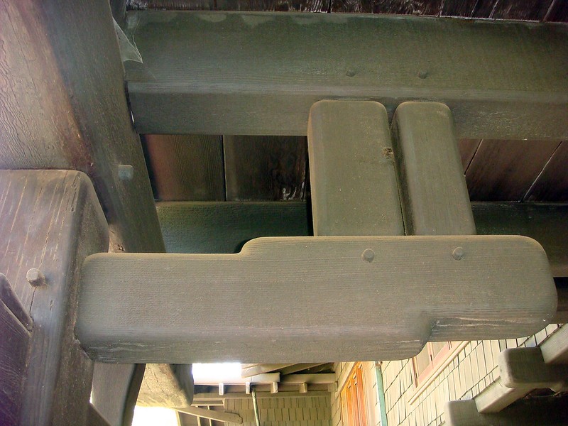 Close-up detail of exposed structural timber connections at the David B. Gamble House, showing rounded shaped beam ends, expressed wooden pegs, and the layered cantilevered roof structure viewed from below
