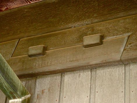 Close-up detail of an exterior Greene and Greene scarf joint where two structural timber members meet end-to-end with a shaped stepped overlap and expressed wooden keys locking the connection