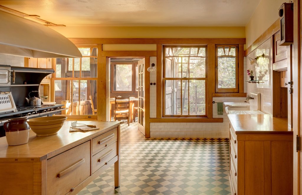 Photograph of the kitchen of the David B. Gamble House showing the maple cabinetry and work surfaces, white subway tile, original cast iron range, and period checkered floor — maple rather than teak because the work done here demanded different material properties