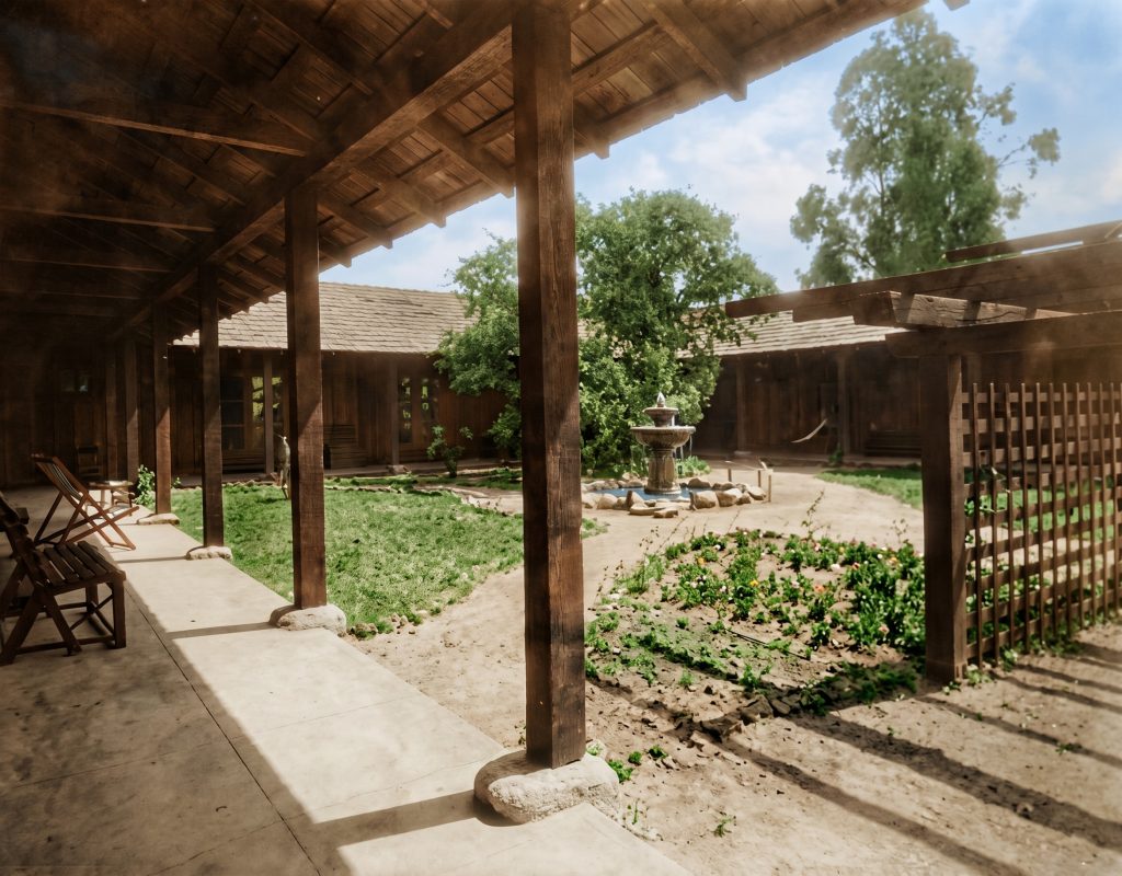 A colorized historic photograph of a U-shaped single-story house enclosing a courtyard with covered walkways on three sides.