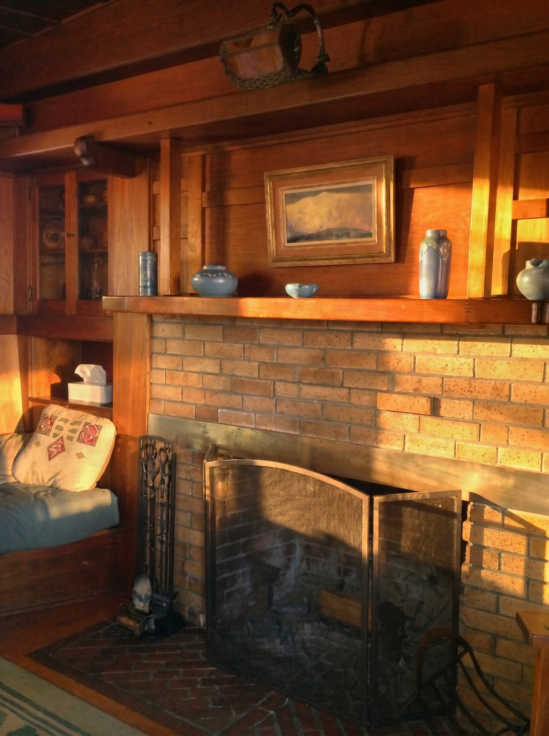 The living-room fireplace of the Charles M. Pratt House near Ojai, a low tiled hearth set in wood paneling with built-in seating, in a rustic Arts and Crafts interior