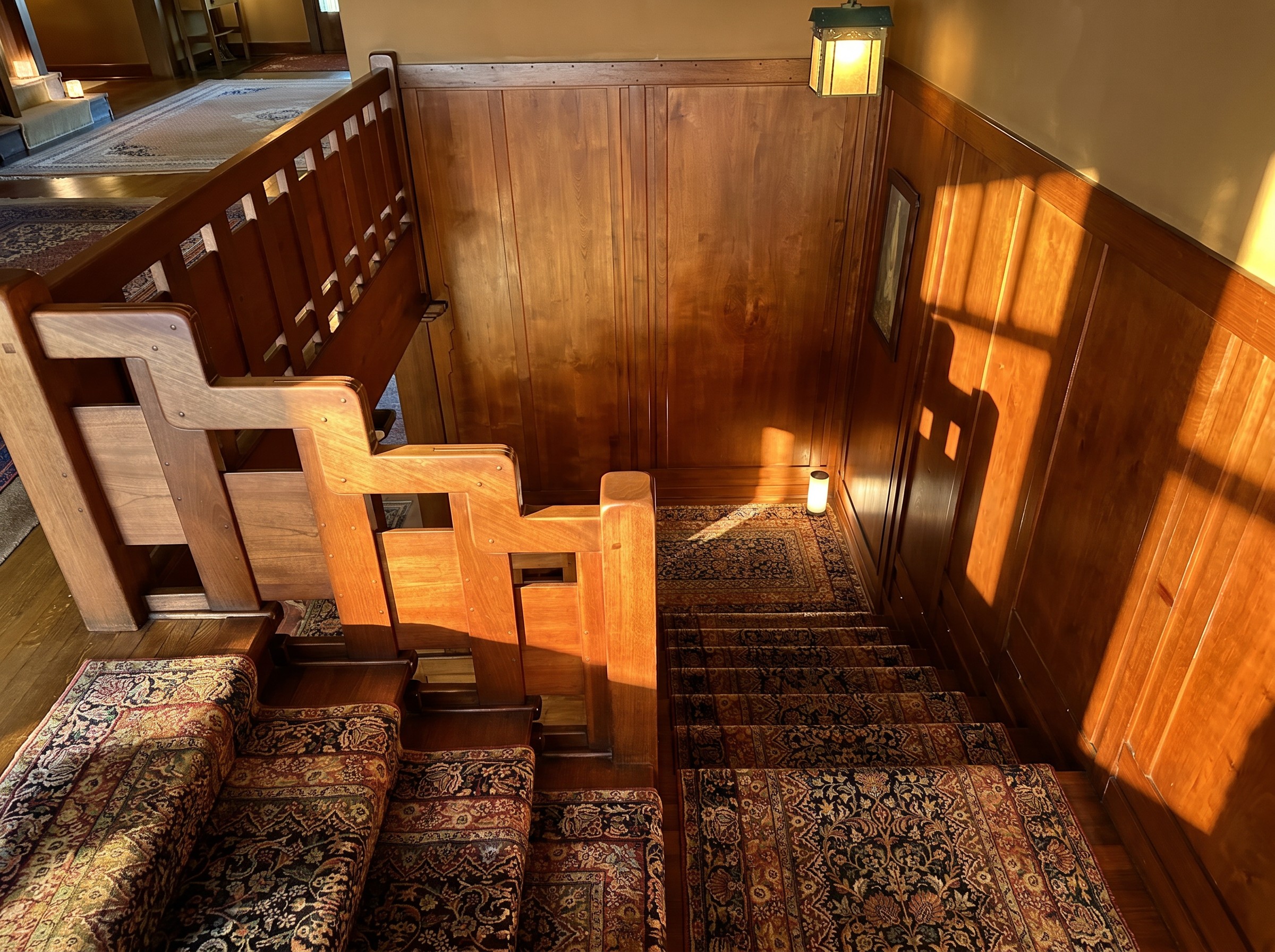 View down the Gamble House staircase from the second floor, showing the stepped teak rail masses descending toward the entrance hall