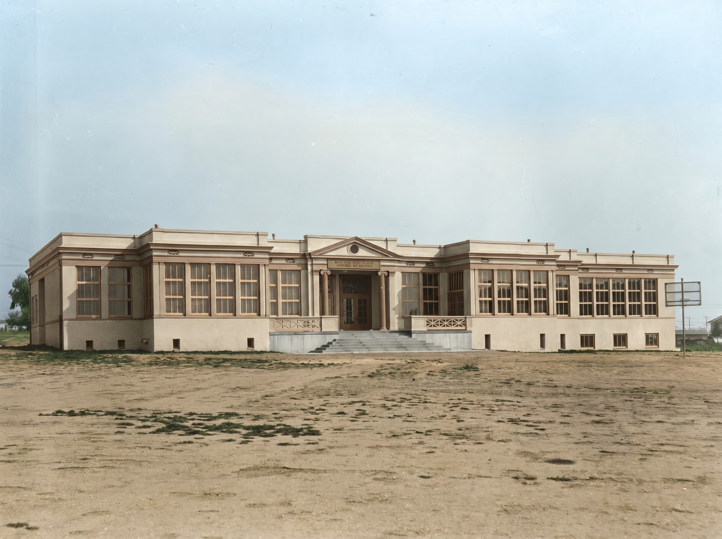 Colorized historic photograph from 1918 showing Longfellow Elementary School shortly after construction, with the pedimented entrance portico, fluted columns, ranks of tall windows, and young landscaping along Washington Boulevard