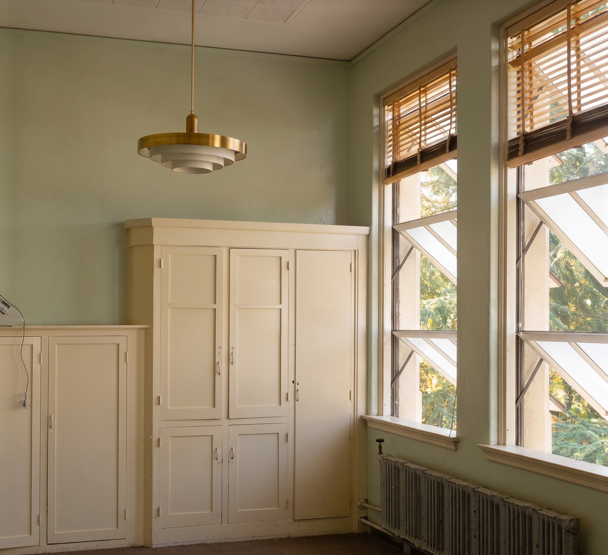 Interior of a Longfellow Elementary School classroom showing tall, generous windows admitting natural daylight across the room, with high ceilings and the plain wood floor characteristic of the building