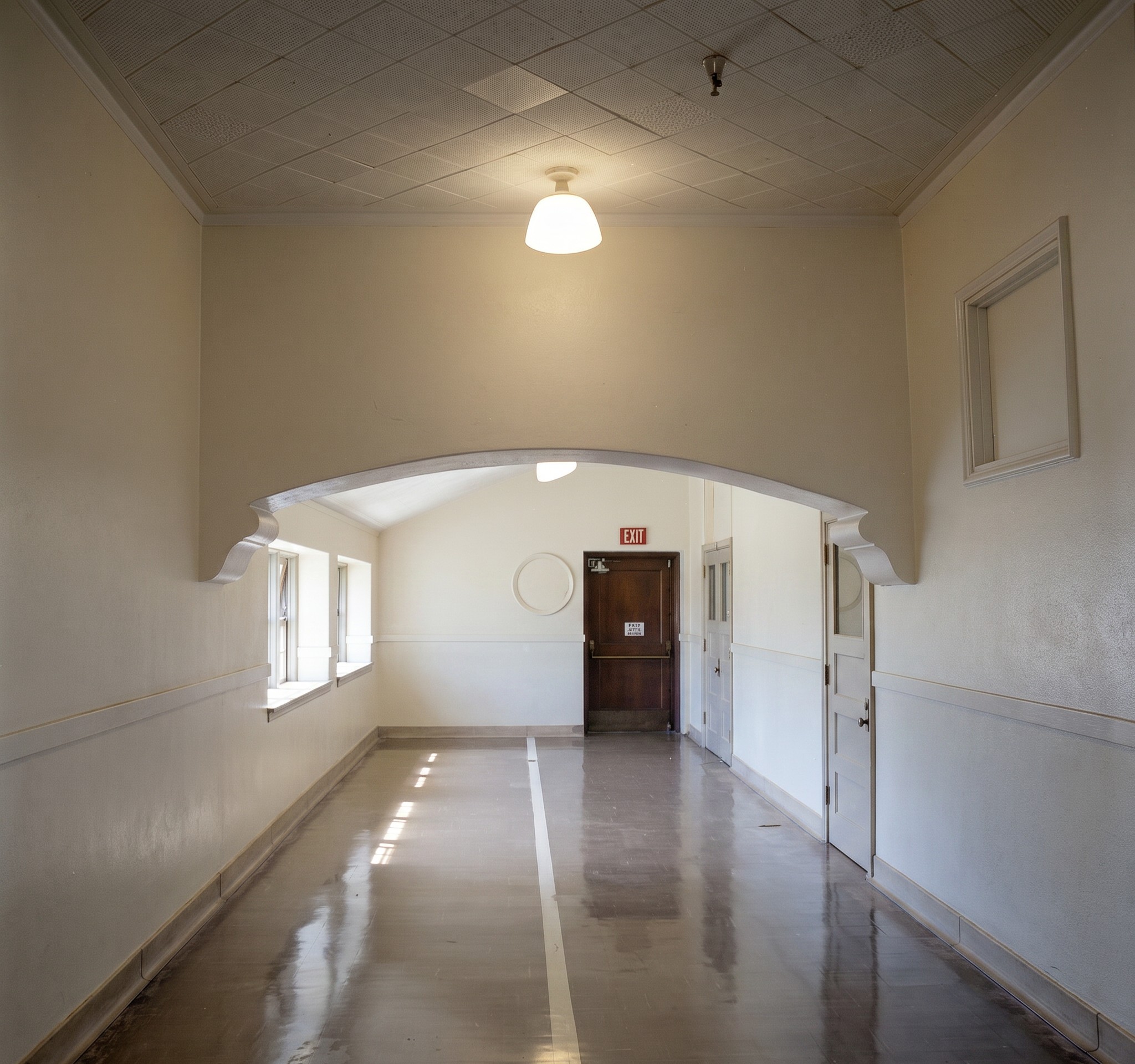 Interior corridor of Longfellow Elementary School showing a wide, well-lit hallway with doors to classrooms, daylight from end windows, and the plain, durable institutional finishes of the building