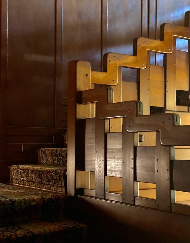 Detail of the Gamble House staircase where the handrail and stringer step downward in stacked bands of teak with inset panels and ebony pegs