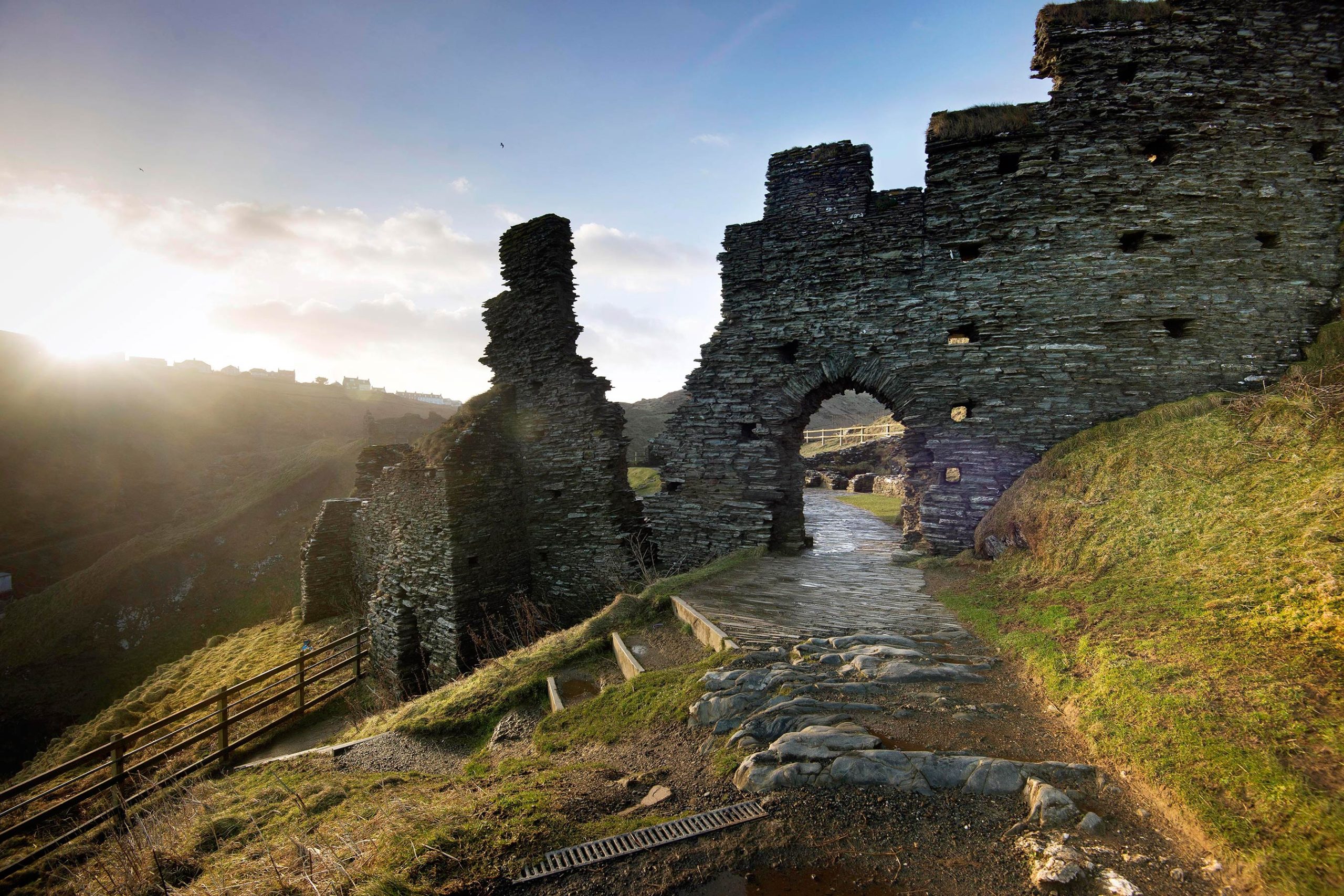 View of Tintagel Castle ruins at sunrise on the granite cliffs of the north Cornwall coast, with stone walls and headland integrated into a single composition above the Atlantic Ocean
